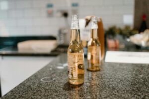 Two bottles of beer on a sleek granite counter with a blurred kitchen background.