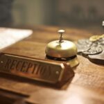 Old fashioned golden service bell and reception sign placed on wooden counter of hotel with retro interior