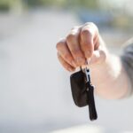 Close-up of a hand handing over car keys, signifying purchase or rental.