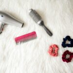 Flatlay of hairstyling tools including a hairdryer, brush, comb, and scrunchies on white fur.